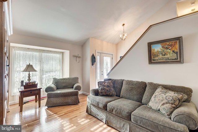 living area featuring baseboards, lofted ceiling, light wood-style floors, and a chandelier