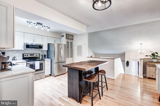 kitchen featuring a breakfast bar area, wooden counters, light wood-style flooring, stainless steel appliances, and backsplash