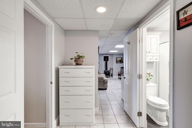 hall featuring light tile patterned floors, baseboards, and a paneled ceiling