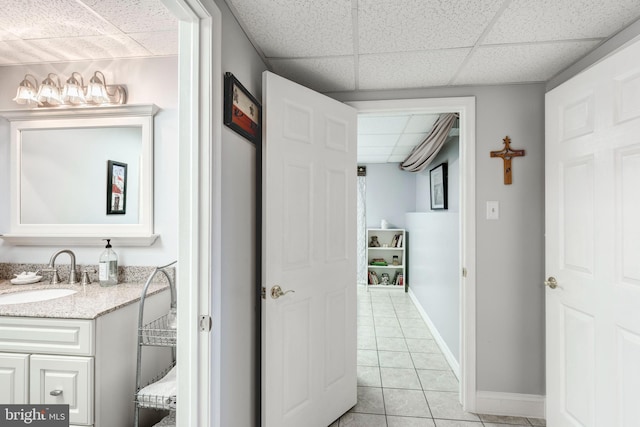 corridor with light tile patterned floors, a paneled ceiling, baseboards, and a sink