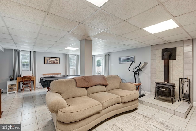 living area with light tile patterned floors, a paneled ceiling, and a wood stove