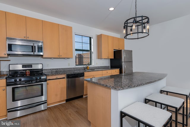 kitchen with dark wood-type flooring, a kitchen breakfast bar, dark stone countertops, appliances with stainless steel finishes, and a chandelier