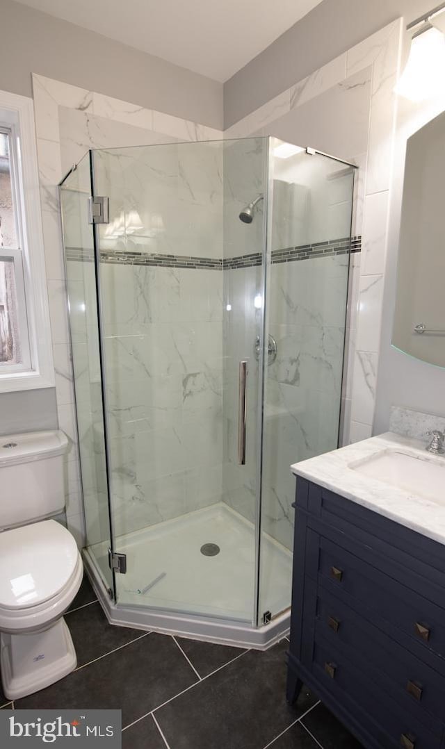 bathroom featuring tile patterned flooring, vanity, an enclosed shower, and toilet