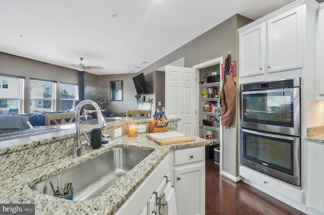 kitchen with light stone counters, ceiling fan, double oven, sink, and white cabinetry