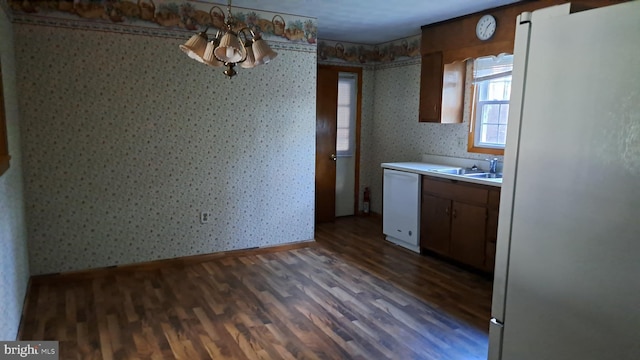 kitchen with white appliances, dark hardwood / wood-style floors, a notable chandelier, and sink