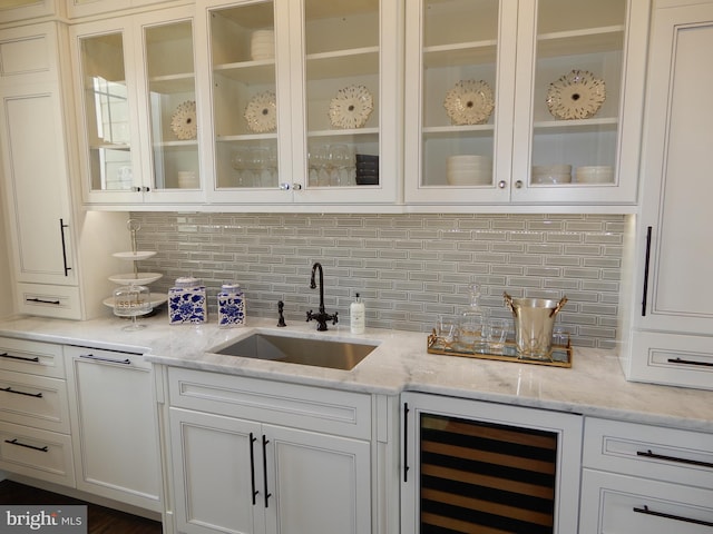 bar with sink, light stone countertops, backsplash, and beverage cooler