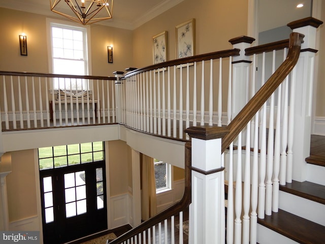 staircase featuring a wealth of natural light, crown molding, and a chandelier