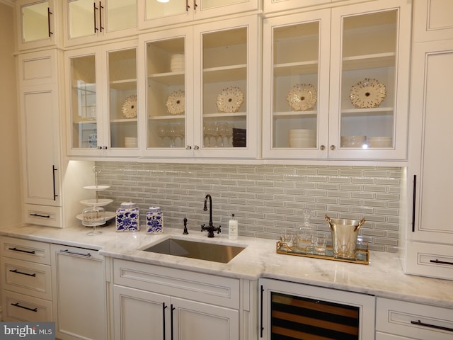 bar with backsplash, light stone countertops, sink, and beverage cooler