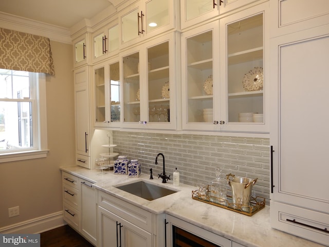 bar with light stone countertops, tasteful backsplash, crown molding, sink, and white cabinetry