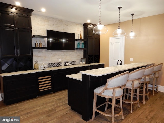 bar featuring backsplash, light hardwood / wood-style floors, light stone countertops, and hanging light fixtures