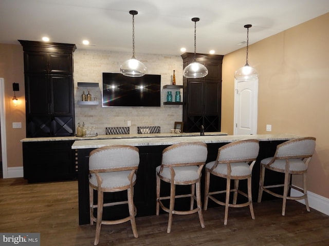 bar with tasteful backsplash, decorative light fixtures, light stone counters, and dark hardwood / wood-style floors