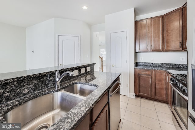 kitchen featuring sink, stainless steel appliances, dark stone counters, dark brown cabinets, and light tile patterned floors