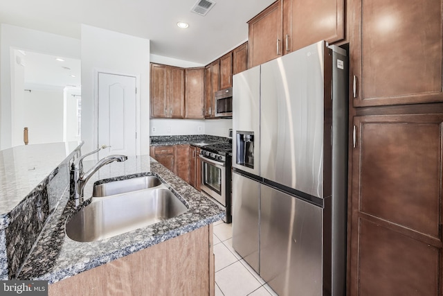 kitchen with light tile patterned flooring, sink, appliances with stainless steel finishes, and dark stone counters