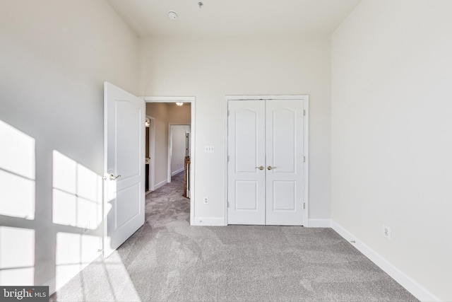 unfurnished bedroom with light colored carpet, a towering ceiling, and a closet