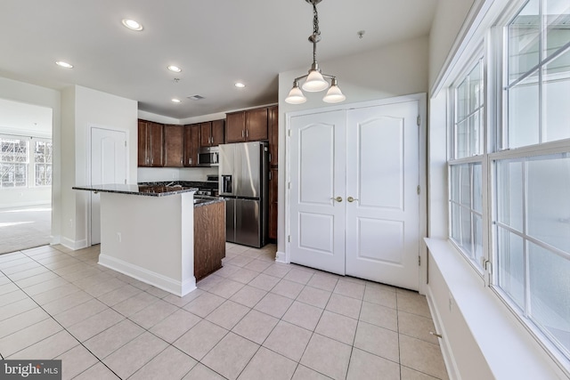 kitchen with dark brown cabinets, stainless steel appliances, pendant lighting, light tile patterned floors, and dark stone countertops