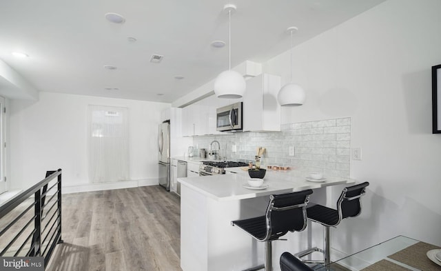 kitchen featuring stainless steel appliances, kitchen peninsula, pendant lighting, a kitchen bar, and white cabinets