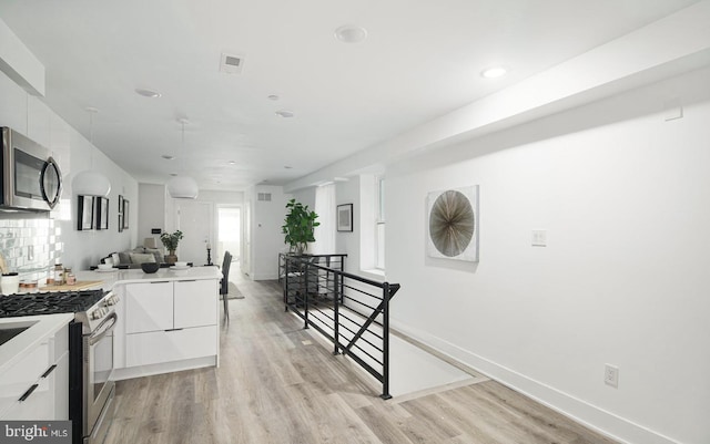 kitchen with decorative backsplash, white cabinetry, light hardwood / wood-style flooring, and appliances with stainless steel finishes