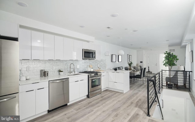 kitchen featuring white cabinets, sink, appliances with stainless steel finishes, decorative light fixtures, and kitchen peninsula