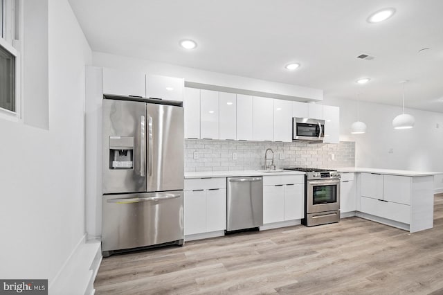 kitchen featuring sink, kitchen peninsula, decorative light fixtures, white cabinets, and appliances with stainless steel finishes