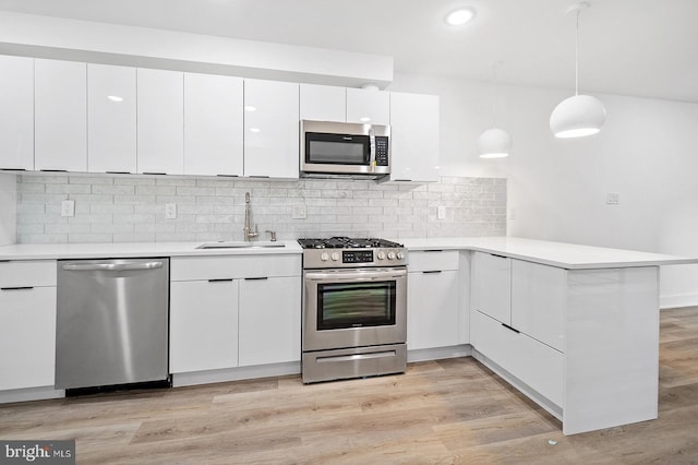 kitchen featuring pendant lighting, sink, kitchen peninsula, appliances with stainless steel finishes, and white cabinetry