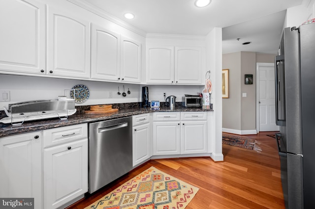 kitchen with stainless steel appliances, white cabinetry, dark stone countertops, and light hardwood / wood-style floors