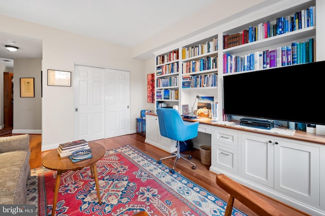 home office featuring built in shelves, built in desk, and dark hardwood / wood-style flooring