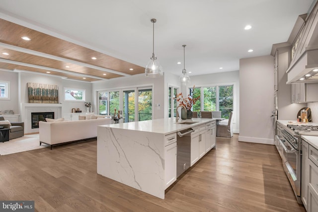 kitchen with a high end fireplace, appliances with stainless steel finishes, light stone counters, sink, and a large island with sink