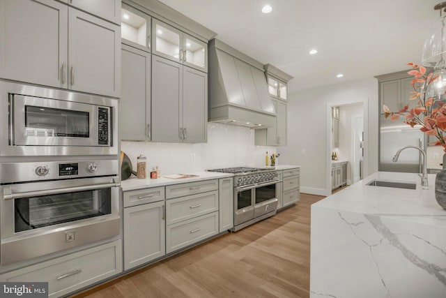 kitchen featuring appliances with stainless steel finishes, custom exhaust hood, sink, decorative light fixtures, and gray cabinets