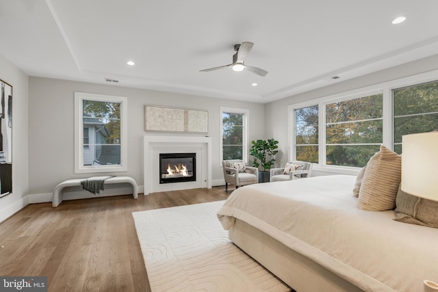 bedroom with ceiling fan, a raised ceiling, and light wood-type flooring