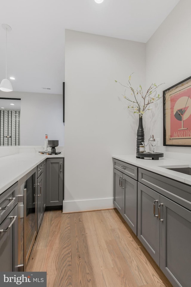 bar with gray cabinetry, light hardwood / wood-style flooring, and hanging light fixtures