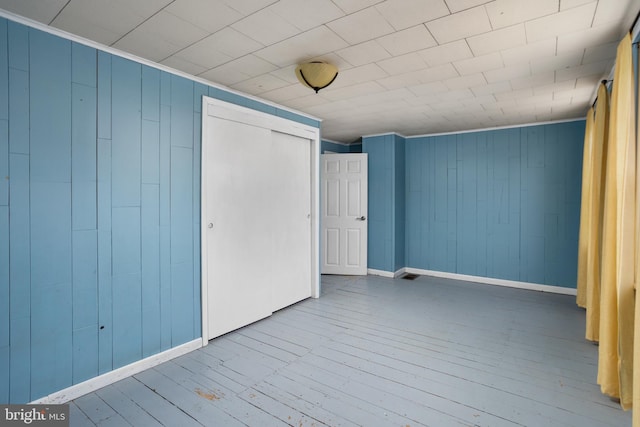 unfurnished bedroom featuring wood walls, wood-type flooring, crown molding, and a closet