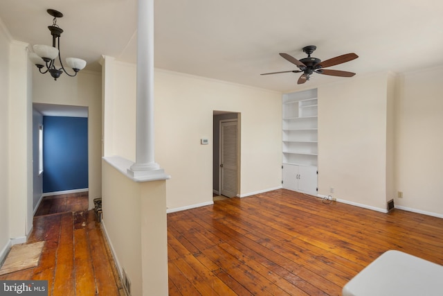 living room featuring built in shelves, dark hardwood / wood-style floors, crown molding, and ceiling fan with notable chandelier