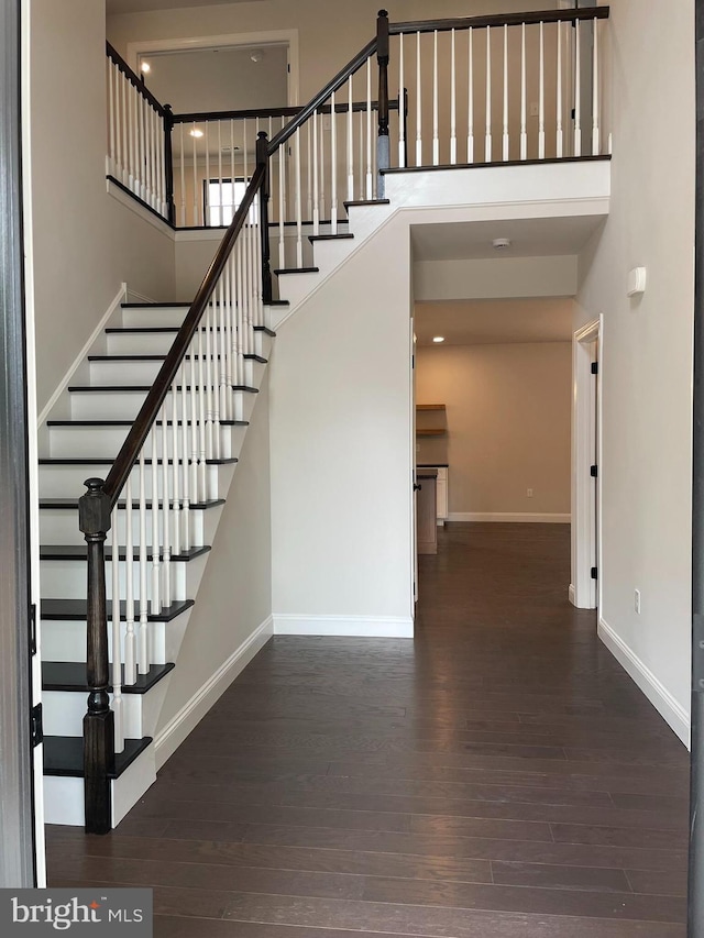 stairway with hardwood / wood-style floors and a towering ceiling