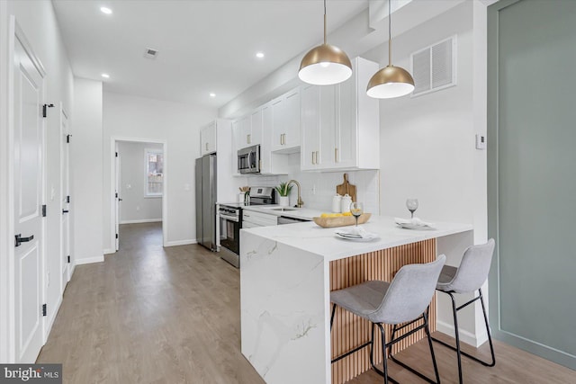 kitchen featuring light stone countertops, appliances with stainless steel finishes, pendant lighting, white cabinetry, and a breakfast bar area