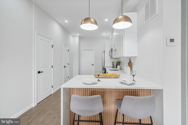 kitchen with white cabinetry, sink, a kitchen breakfast bar, kitchen peninsula, and pendant lighting