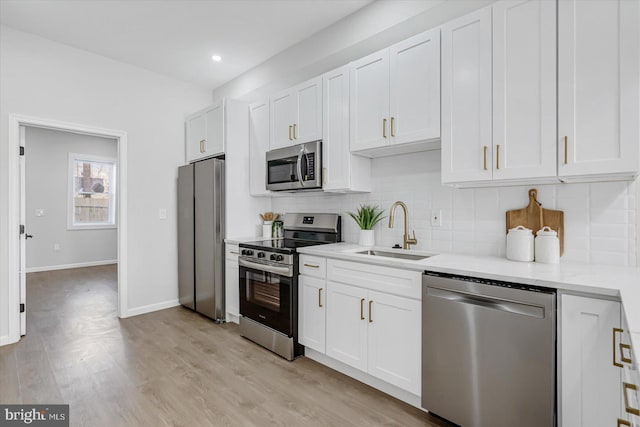 kitchen featuring sink, light wood-type flooring, light stone counters, white cabinetry, and stainless steel appliances