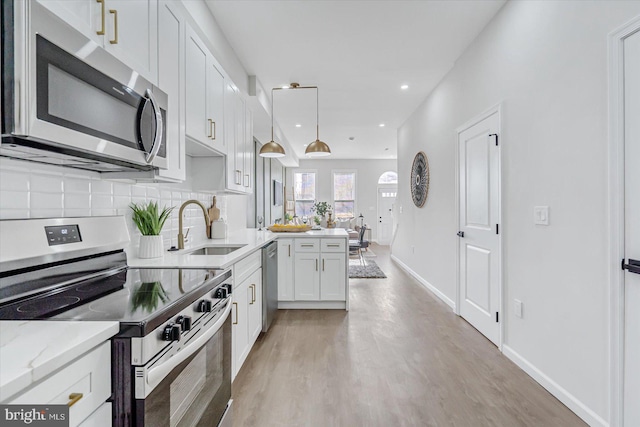 kitchen with light stone countertops, sink, decorative light fixtures, white cabinets, and appliances with stainless steel finishes