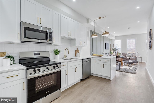 kitchen featuring kitchen peninsula, appliances with stainless steel finishes, sink, pendant lighting, and white cabinets