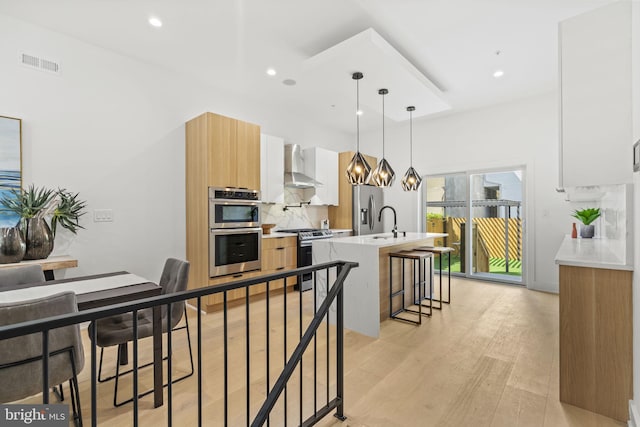 kitchen with white cabinetry, wall chimney exhaust hood, hanging light fixtures, a breakfast bar area, and appliances with stainless steel finishes