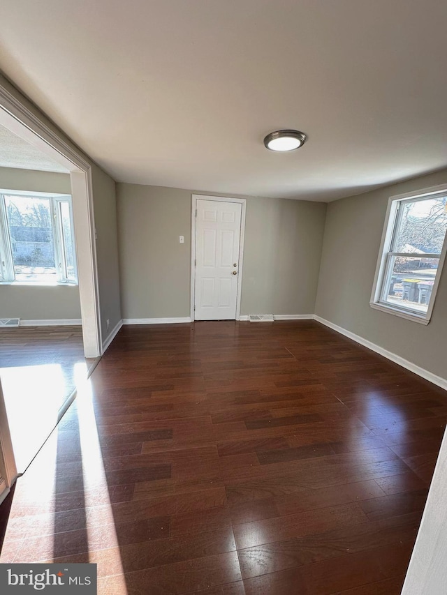 empty room featuring a healthy amount of sunlight and dark wood-type flooring