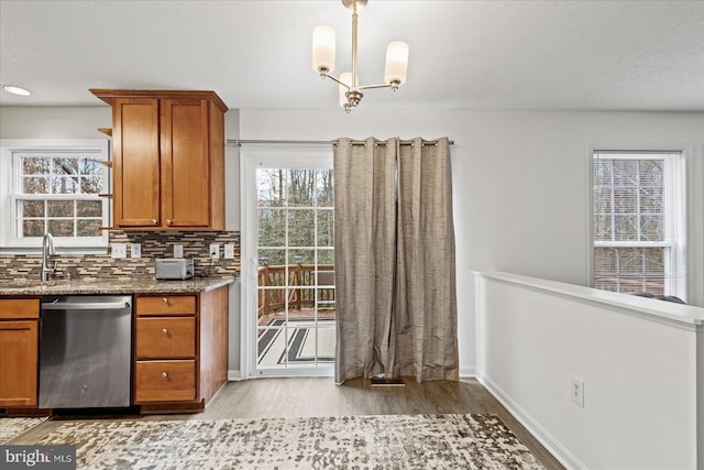 kitchen featuring light stone countertops, sink, stainless steel dishwasher, a notable chandelier, and decorative backsplash