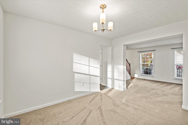 carpeted empty room featuring a textured ceiling and an inviting chandelier