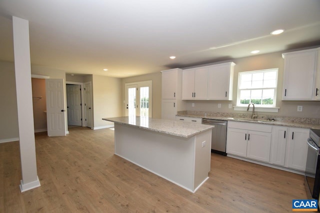 kitchen with stainless steel dishwasher, light wood-type flooring, a kitchen island, light stone counters, and white cabinetry