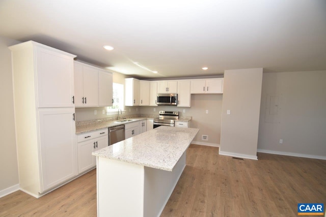 kitchen with light stone countertops, white cabinetry, a center island, stainless steel appliances, and sink