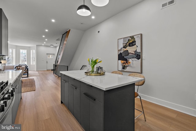 kitchen with light wood finished floors, stainless steel gas range oven, a kitchen island, and visible vents