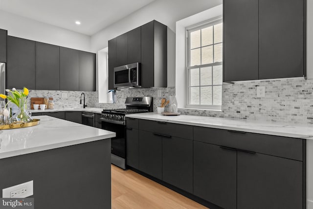 kitchen featuring stainless steel appliances, modern cabinets, decorative backsplash, and light wood-style floors