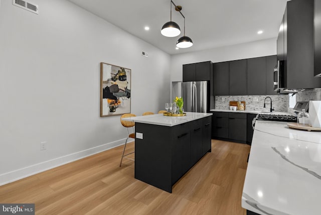 kitchen with dark cabinets, a kitchen island, appliances with stainless steel finishes, light wood finished floors, and decorative light fixtures