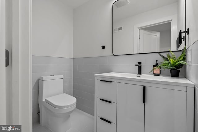 bathroom featuring visible vents, wainscoting, toilet, vanity, and tile walls