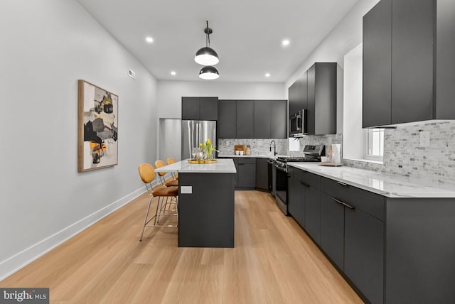 kitchen featuring a breakfast bar, pendant lighting, light wood-style flooring, appliances with stainless steel finishes, and a kitchen island