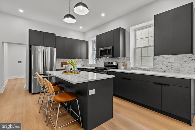 kitchen with a kitchen breakfast bar, a center island, hanging light fixtures, stainless steel appliances, and dark cabinetry